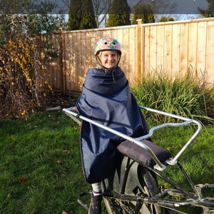 May include: A dark blue weather-resistant cover draped over a bicycle seat and frame, featuring a smooth, water-repellent surface. The cover is secured around the seat area, providing protection for the bicycle components from outdoor elements.