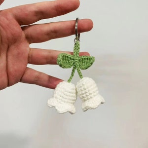 May include: White crocheted lily of the valley flower keychain with green leaves and a silver key ring.