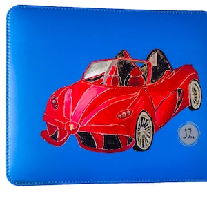 May include: A red convertible sports car painted on a blue leather laptop sleeve. The car has a black interior and black wheels. The sleeve has a white stitched border and the artist's signature "JZ" in a circle.