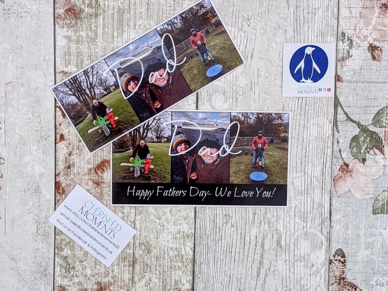 May include: A card with a photo collage of a father and his children. The card has the text "Dad" written in cursive and "Happy Fathers Day- We Love You!" printed below the photos. The card is on a wooden surface with a floral pattern.