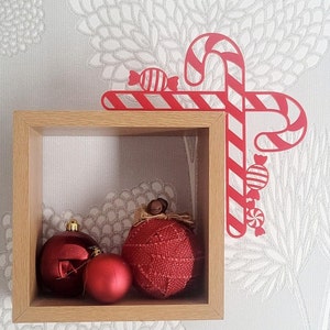 May include: A wooden shelf with three red ornaments, two round and one heart-shaped, and a red and white candy cane decoration.