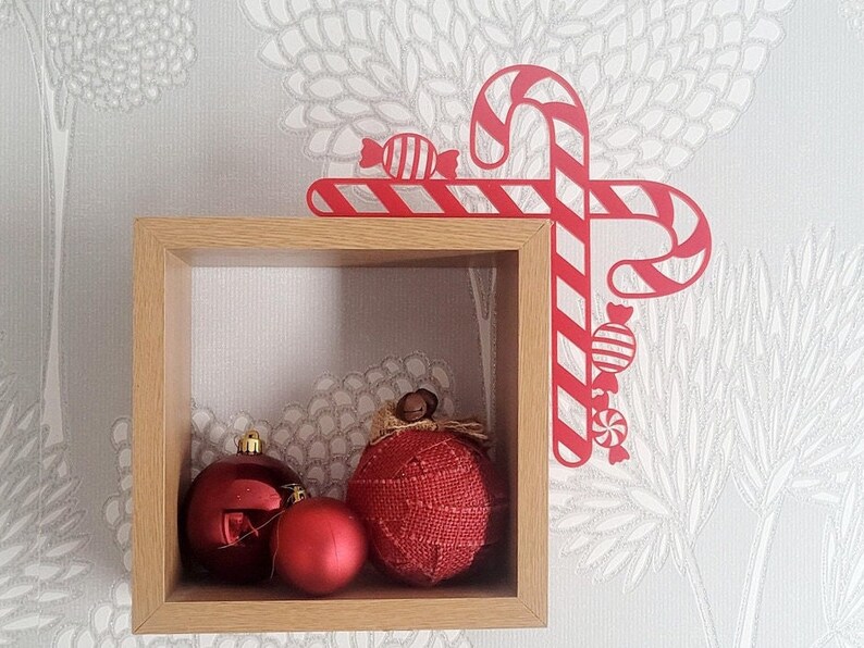 May include: A wooden shelf with three red ornaments, two round and one heart-shaped, and a red and white candy cane decoration.