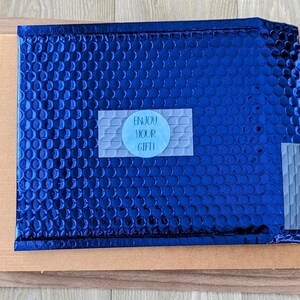 May include: A blue padded envelope with a white sticker that says "Enjoy your gift!"