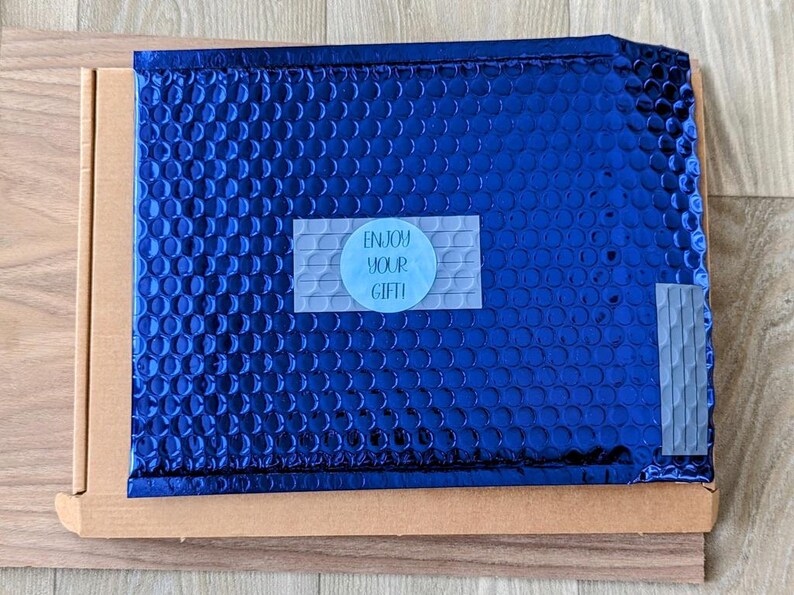 May include: A blue padded envelope with a white sticker that says "Enjoy your gift!"
