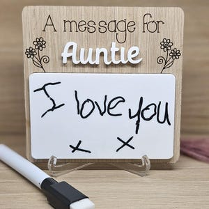 May include: A wooden sign with a white dry-erase board that says "A message for Auntie I love you" with two Xs below the message. The sign has a floral design on the top and bottom.