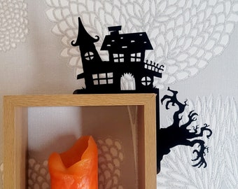Può includere: Mensola a muro in metallo nero a forma di casa infestata con un ramo d'albero. La mensola è montata su uno scaffale in legno con una candela arancione all'interno.