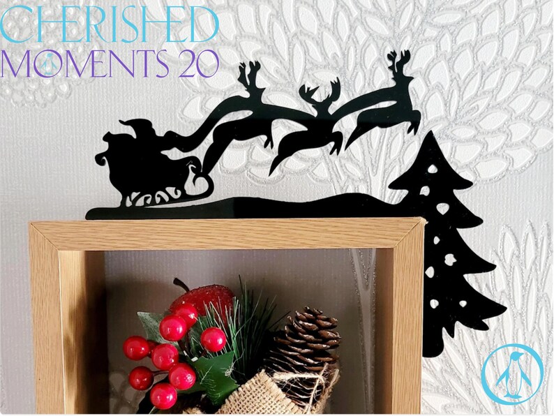 May include: Black metal silhouette of Santa Claus in a sleigh pulled by reindeer flying over a Christmas tree. The silhouette is mounted on a wooden shelf with a Christmas-themed decoration in the foreground.