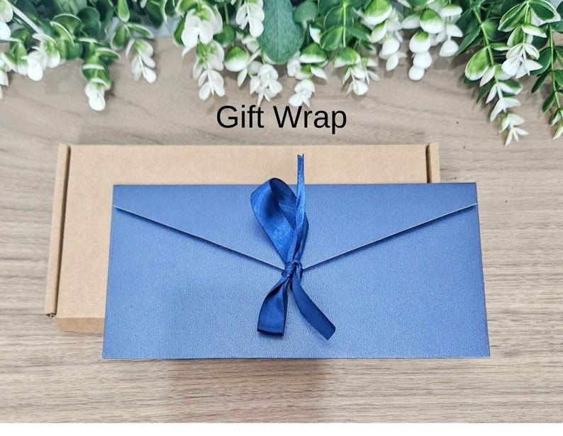 May include: A blue envelope with a blue ribbon tied in a bow. The envelope is on a wooden surface with the text "Gift Wrap" above it.