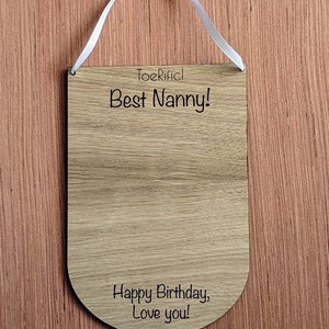 K&ouml;nnte beinhalten: Holzschilder mit einem wei&szlig;en Band zum Aufh&auml;ngen. Das Schild lautet "Toerific! Best Nanny! Happy Birthday, Love you!"