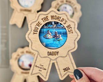 May include: Wooden photo frame shaped like a ribbon with the text "You're the world's best Daddy" and a photo of a family at a pool. The frame also includes the text "Love Bertie & Caleb 2024".