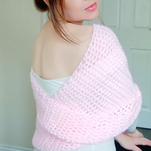 May include: A pink crocheted shrug with a loose, open weave. The shrug is draped over the shoulders and has a V-neckline.