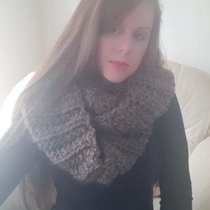 May include: A woman wearing a gray knitted infinity scarf and a black long-sleeved shirt.