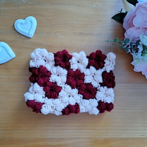 Puede incluir: Un cuadrado tejido a crochet con un patrón repetido de flores de color burdeos y crema.