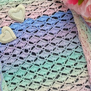 May include: A pastel rainbow crochet shawl with a delicate, lacy pattern. The shawl is decorated with two white ceramic hearts.