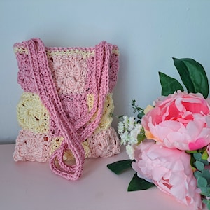 May include: A crocheted handbag with a pink and yellow color scheme. The bag has a single strap and is made with a circular stitch pattern.