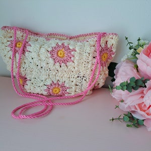 May include: A crocheted bag with a pink strap and white and pink flower designs.