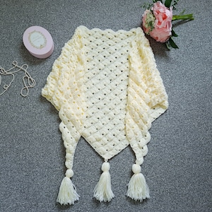 May include: A crocheted shawl with a delicate, lacy pattern in a soft cream color. The shawl has three tassels at the bottom, adding a touch of elegance.
