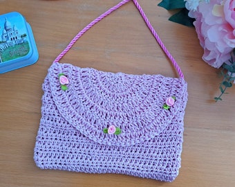 May include: A lavender crocheted purse with a pink strap and pink flower embellishments.