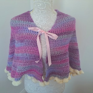 May include: A purple and pink striped crocheted shawl with a white crocheted trim and a pink satin ribbon tied around the neck.