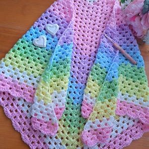 May include: A rainbow crochet baby blanket with a scalloped edge. The blanket is made with a variety of pastel colors, including pink, blue, green, and yellow.