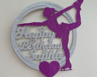 May include: A silver glitter cake topper with a purple glitter silhouette of a figure skater. The topper says "Happy Birthday Sophie" and has a purple glitter heart.