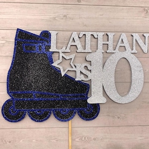 May include: A glittery cake topper featuring a black and blue inline skate next to the silver text LATHAN IS 10 with a star icon. The design is constructed from layered cardstock with a textured finish and is attached to a thin wooden stick.