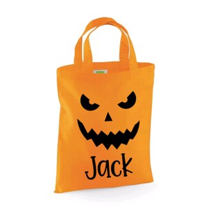 Puede incluir: Bolsa de truco o trato de Halloween naranja con una cara de calabaza negra y el nombre "Jack" impreso en la parte delantera.