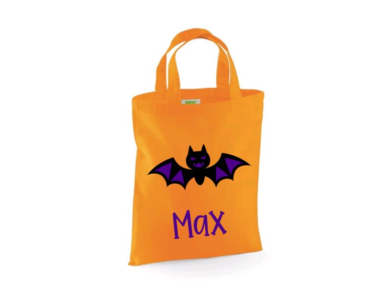 Puede incluir: Bolsa naranja de truco o trato de Halloween con un murci&eacute;lago negro y alas moradas. La bolsa tiene el nombre "Max" impreso en ella.