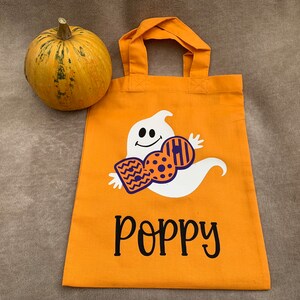 Puede incluir: Bolsa naranja de truco o trato de Halloween con un fantasma sosteniendo un cartel de "BOO" y el nombre "Poppy" impreso en la parte delantera.