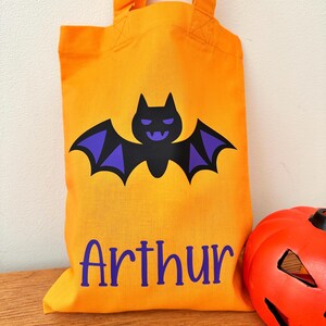 Puede incluir: Bolsa de truco o trato de Halloween naranja con un murci&eacute;lago morado y el nombre "Arthur" impreso en la parte delantera.
