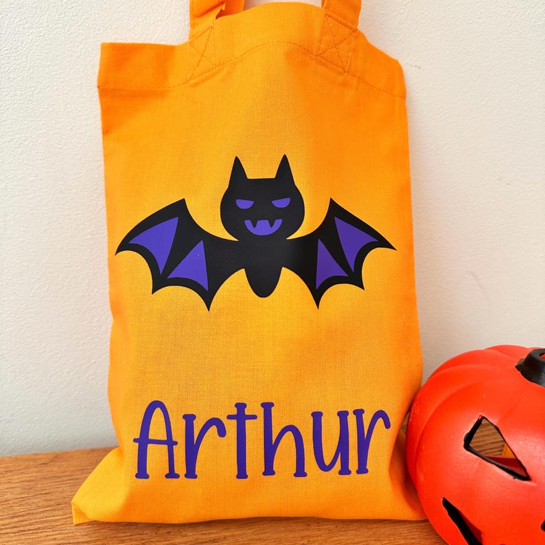 Puede incluir: Bolsa de truco o trato de Halloween naranja con un murci&eacute;lago morado y el nombre "Arthur" impreso en la parte delantera.