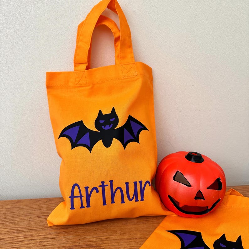 Puede incluir: Bolsa de truco o trato de Halloween naranja con un murci&eacute;lago morado y el nombre "Arthur" impreso en la parte delantera.