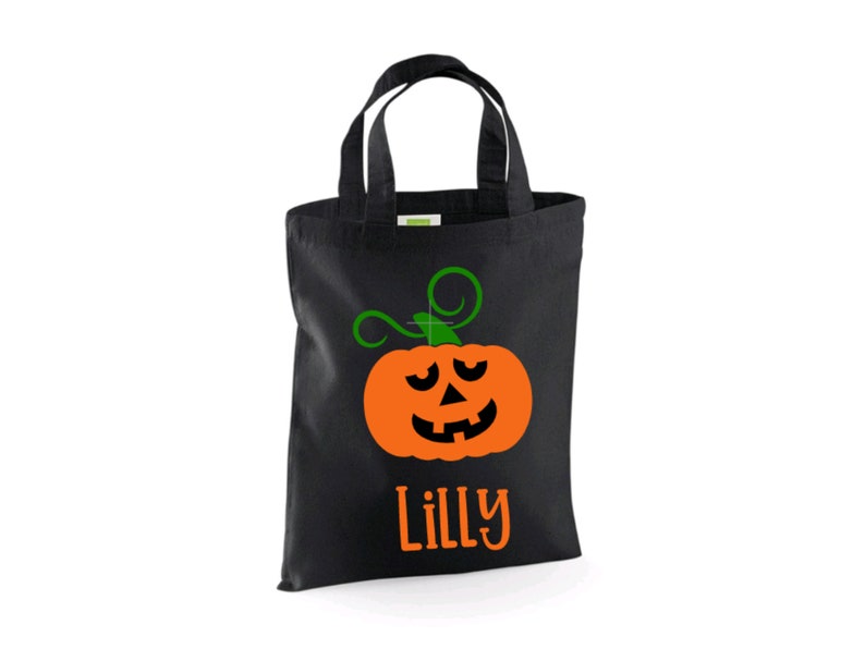 Puede incluir: Bolsa negra de truco o trato con una cara de calabaza verde y naranja y el nombre "Lilly" impreso en la parte delantera.