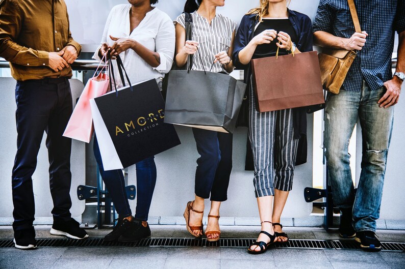 May include: Five people are holding shopping bags. The bags are various colors and sizes. One bag has the text "AMORE COLLECTION" printed on it.