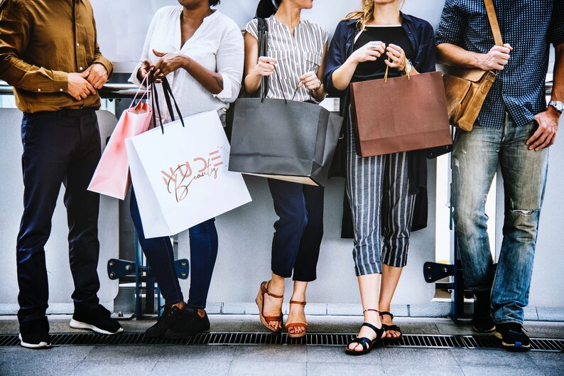 May include: Five people are holding shopping bags. The bags are various colors and sizes. One bag has the text "Wilde Beauty" printed on it.