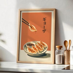 May include: A framed wall art print featuring a burnt orange background with a plate of pan-fried gyoza dumplings and a small bowl of dipping sauce. A pair of black chopsticks holds a single gyoza above the plate. The Japanese text reads ギョーザ.