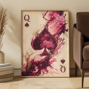 May include: A framed wall art print featuring a Queen of Spades playing card design. The centre displays a large spade symbol surrounded by abstract, flowing splashes of deep burgundy and wine-coloured ink on a textured, vintage-style beige background.