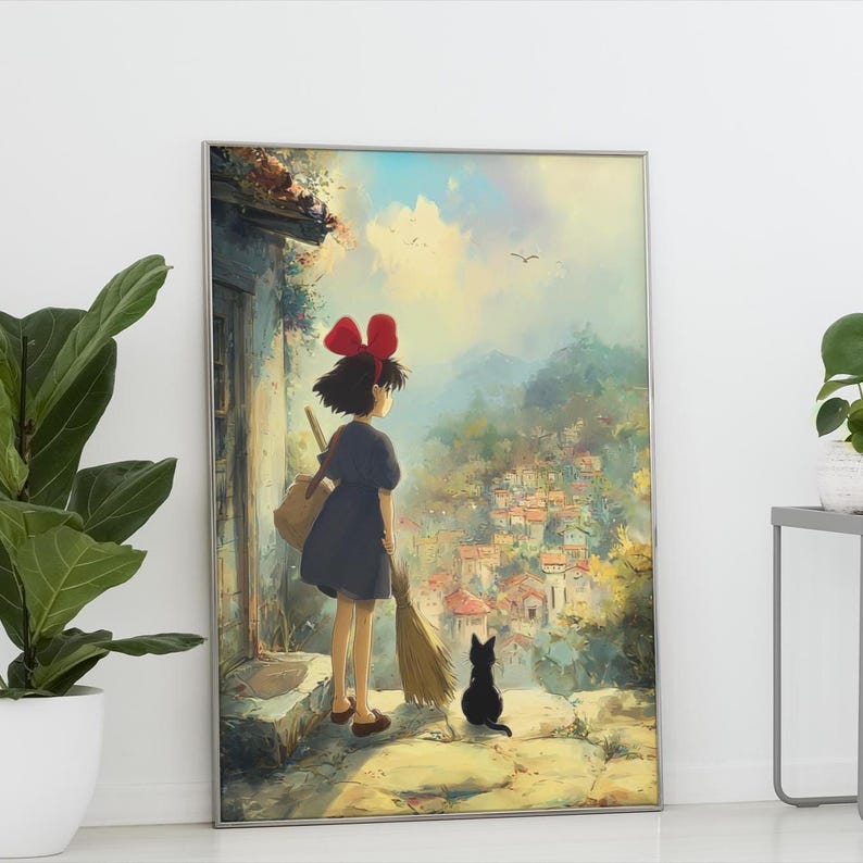 May include: Framed art print featuring a young girl with a red bow, a broom, and a black cat, overlooking a village. The artwork has a soft, painterly style with a vibrant sky and detailed buildings. The print is in a silver frame.