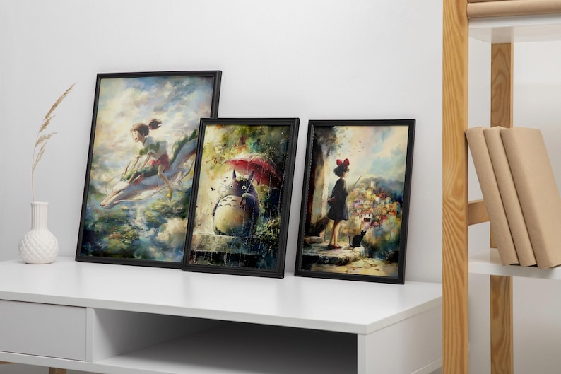 K&ouml;nnte beinhalten: Drei gerahmte Kunstdrucke mit Szenen aus Zeichentrickfilmen. Die Drucke zeigen ein M&auml;dchen, das auf einem Drachen reitet, Totoro unter einem Regenschirm und ein M&auml;dchen mit einer schwarzen Katze. Die Rahmen sind schwarz, und die Drucke werden auf einer wei&szlig;en Oberfl&auml;che pr&auml;sentiert.