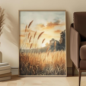 Könnte beinhalten: Ein rechteckiger gerahmter Kunstdruck mit einem Landschaftsgemälde eines goldenen Feldes aus hohem Gras und Schilf unter einem sanften Sonnenuntergangshimmel. Die Szene zeigt Baum-Silhouetten im Hintergrund mit warmen orangefarbenen und gelben Lichttönen.