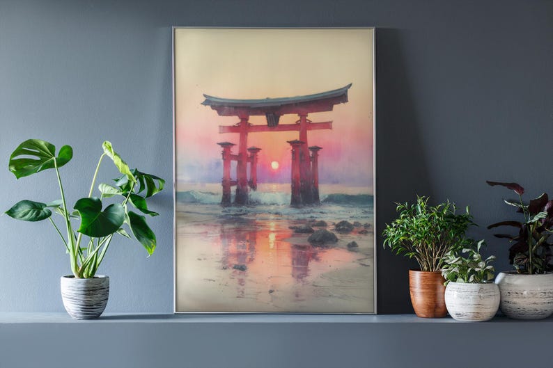 May include: Framed art print of a Japanese Torii gate at sunset. The red gate stands in the ocean, with the sun setting behind it, casting a warm glow. The artwork is displayed on a gray wall, with potted plants in front.