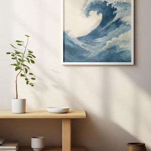 May include: A framed art print featuring a watercolor depiction of a large ocean wave. The wave is rendered in shades of blue and white, with a foamy crest. The artwork is displayed in a white frame against a neutral wall.