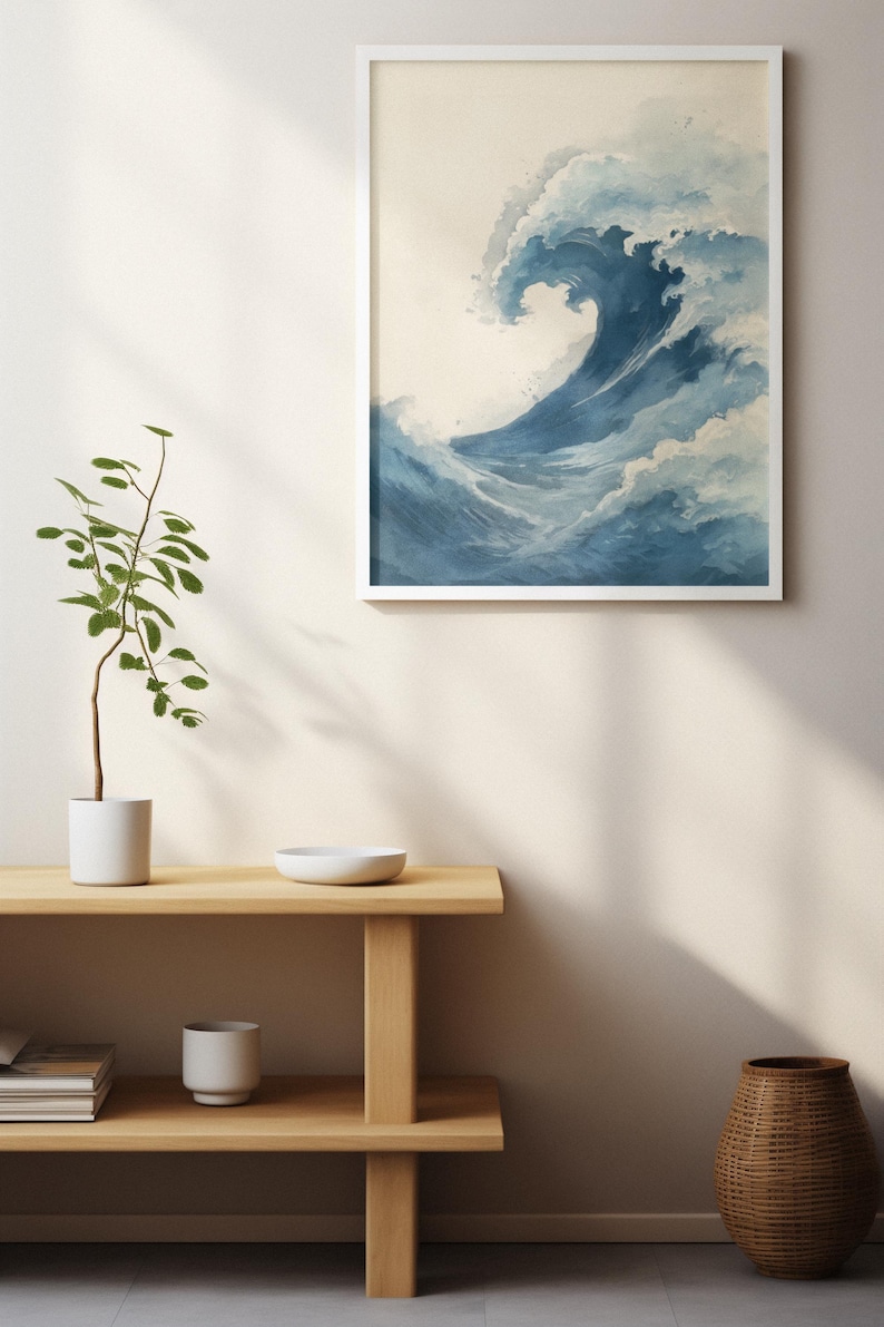 May include: A framed art print featuring a watercolor depiction of a large ocean wave. The wave is rendered in shades of blue and white, with a foamy crest. The artwork is displayed in a white frame against a neutral wall.