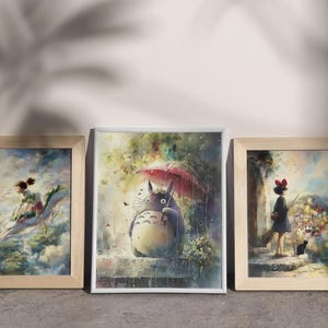 K&ouml;nnte beinhalten: Drei gerahmte Kunstdrucke mit Aquarellillustrationen. Der mittlere Druck zeigt ein gro&szlig;es, graues Wesen mit einem Regenschirm. Die beiden anderen Drucke zeigen Szenen mit Figuren in einem vertr&auml;umten, farbenfrohen Stil, alle in Holz gerahmt.