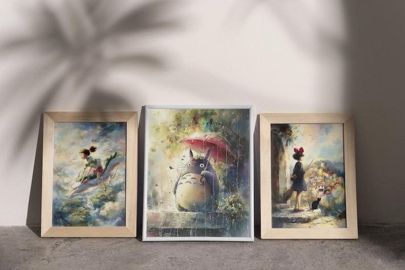 K&ouml;nnte beinhalten: Drei gerahmte Kunstdrucke mit Aquarellillustrationen. Der mittlere Druck zeigt ein gro&szlig;es, graues Wesen mit einem Regenschirm. Die beiden anderen Drucke zeigen Szenen mit Figuren in einem vertr&auml;umten, farbenfrohen Stil, alle in Holz gerahmt.