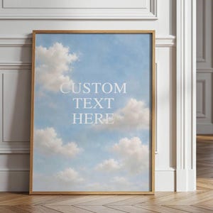 May include: A vertical rectangular wall art print in a light wood frame featuring a clear blue sky with soft white clouds. The centre of the print displays the white text CUSTOM TEXT HERE in a clean, sans-serif font, centred against the sky.