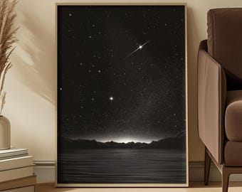 May include: A rectangular framed wall art print featuring a black and white night sky over a calm body of water. The scene depicts a dark horizon with silhouetted mountains, a starry sky with a bright shooting star, and a glowing light source.