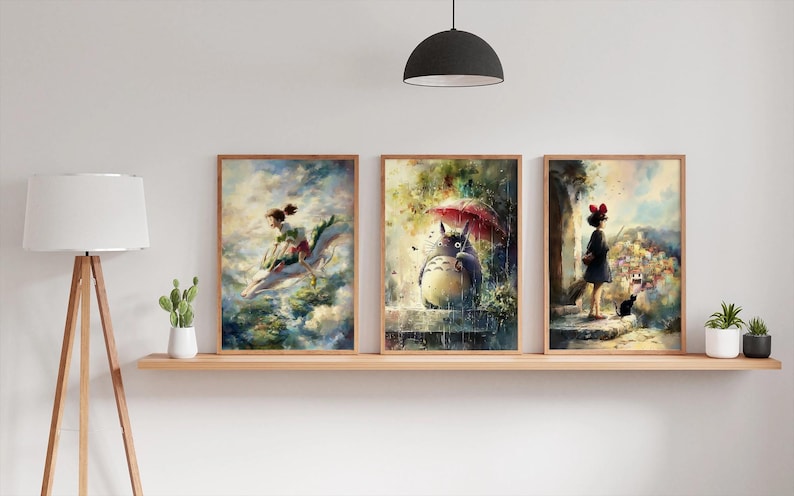 K&ouml;nnte beinhalten: Drei gerahmte Kunstdrucke mit Aquarellillustrationen. Die Drucke zeigen Szenen aus einem Zeichentrickfilm, darunter ein M&auml;dchen, das auf einem Drachen reitet, eine gro&szlig;e Kreatur unter einem Regenschirm und ein M&auml;dchen mit einer schwarzen Katze. Die Rahmen sind hellbraun.