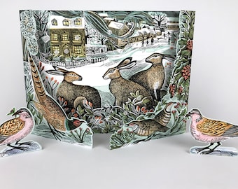May include: A three-dimensional advent calendar featuring a winter village scene with three brown hares in the foreground. Two separate bird cutouts stand on either side, each with pink, brown, and black plumage. The central panel displays numbered doors.