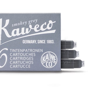 May include: A box of Kaweco smokey grey ink cartridges. The box is gray with white text and a pen nib logo. The text includes "GERMANY, SINCE 1883." and the number "6". Three cartridges are visible.
